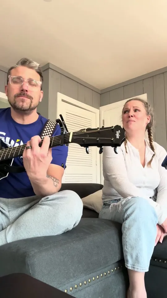 A guitarist and a vocalist from The Straight A's Band performing an acoustic song while seated on a couch
